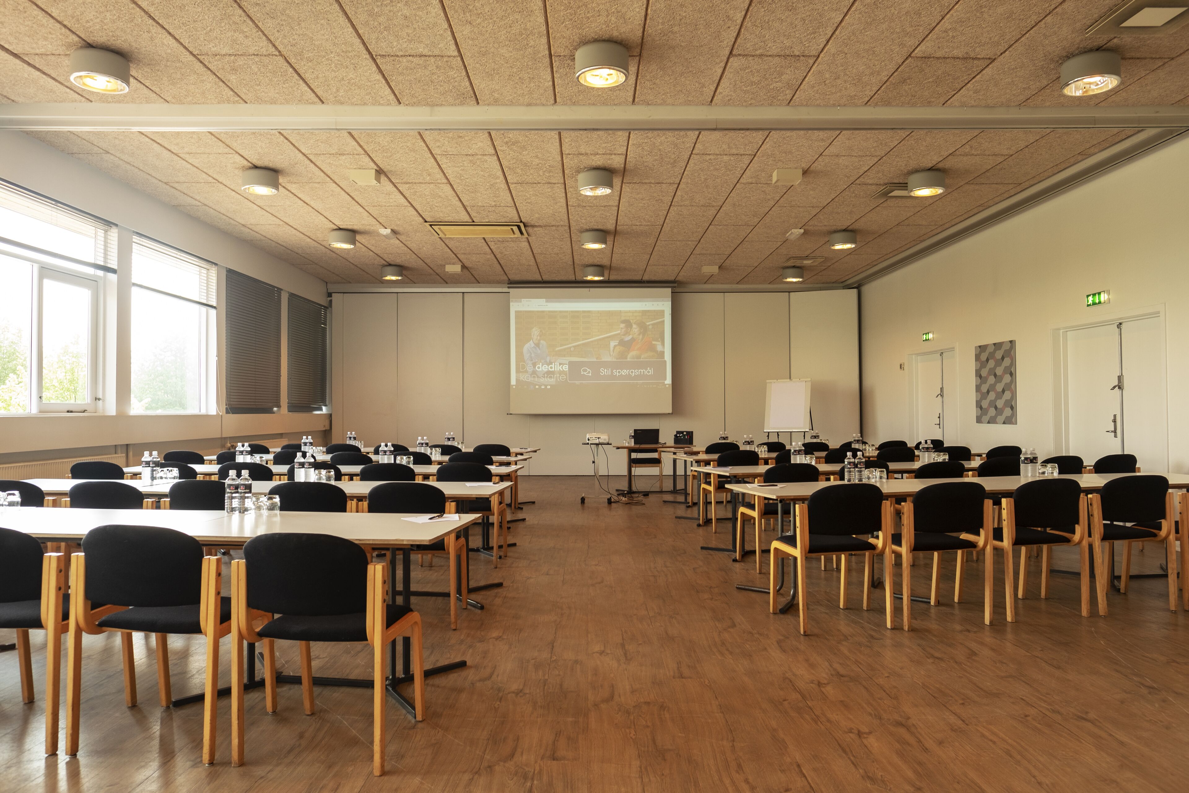 A conference room with multiple tables and chairs, a projector screen, and a presentation on the wall.