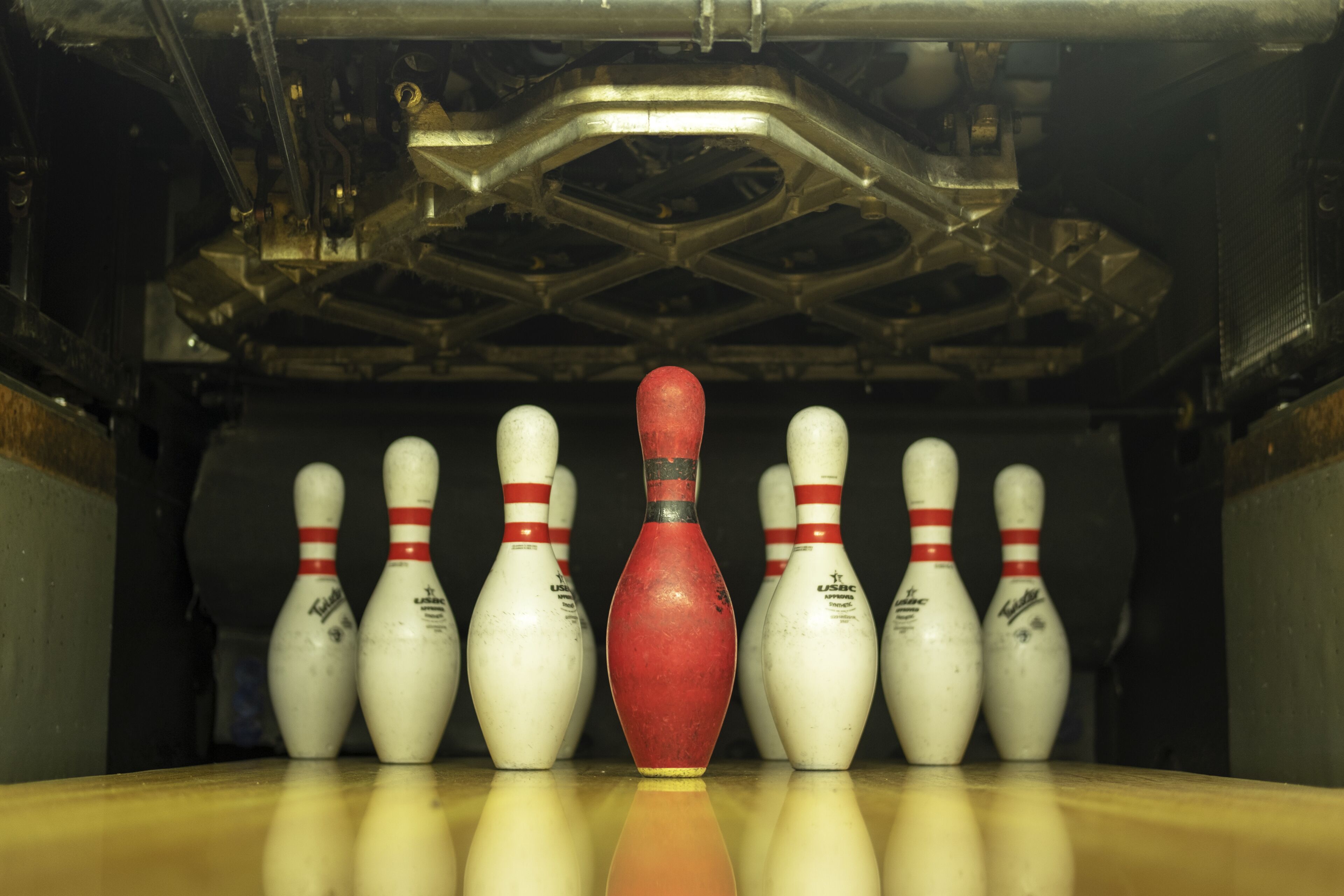 Une salle de bowling avec une quille rouge au centre et plusieurs quilles blanches en arrière-plan.