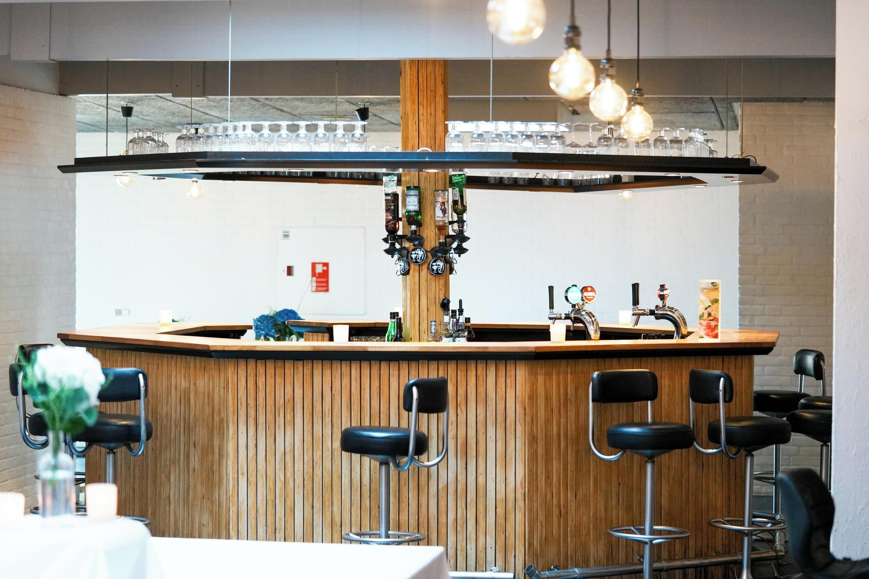 A bar area with a wooden counter, bar stools, and a variety of bottles and glasses.