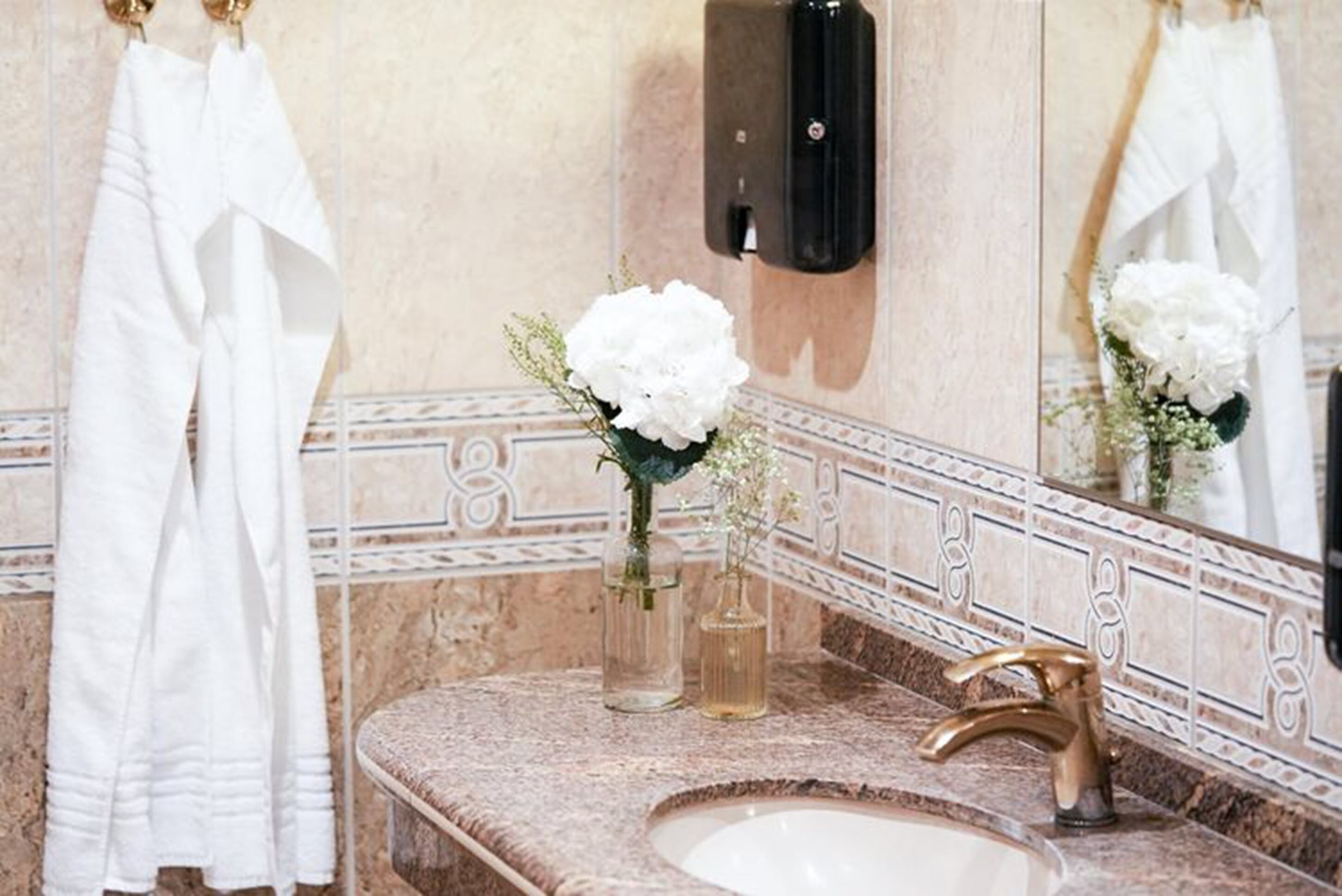 Un baño con lavamanos de mármol, grifo dorado y espejo con detalles de azulejos decorativos.
