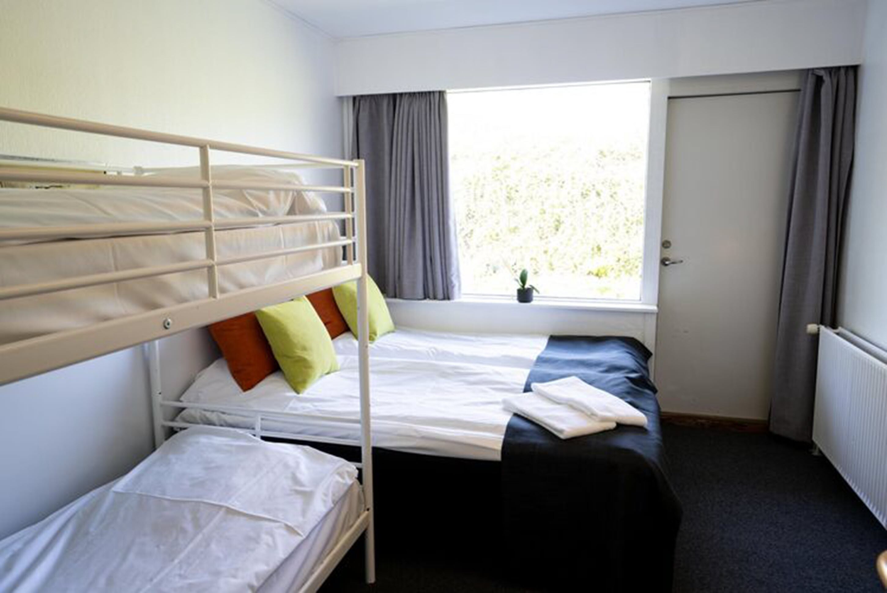 A room with bunk beds, a window with curtains, and a door.
