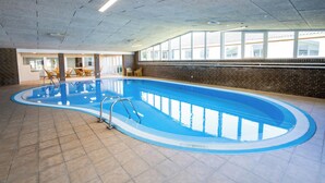 An indoor swimming pool with clear blue water, a tiled floor, and a brick wall. - Hotel Pejsegården (Braedstrup)