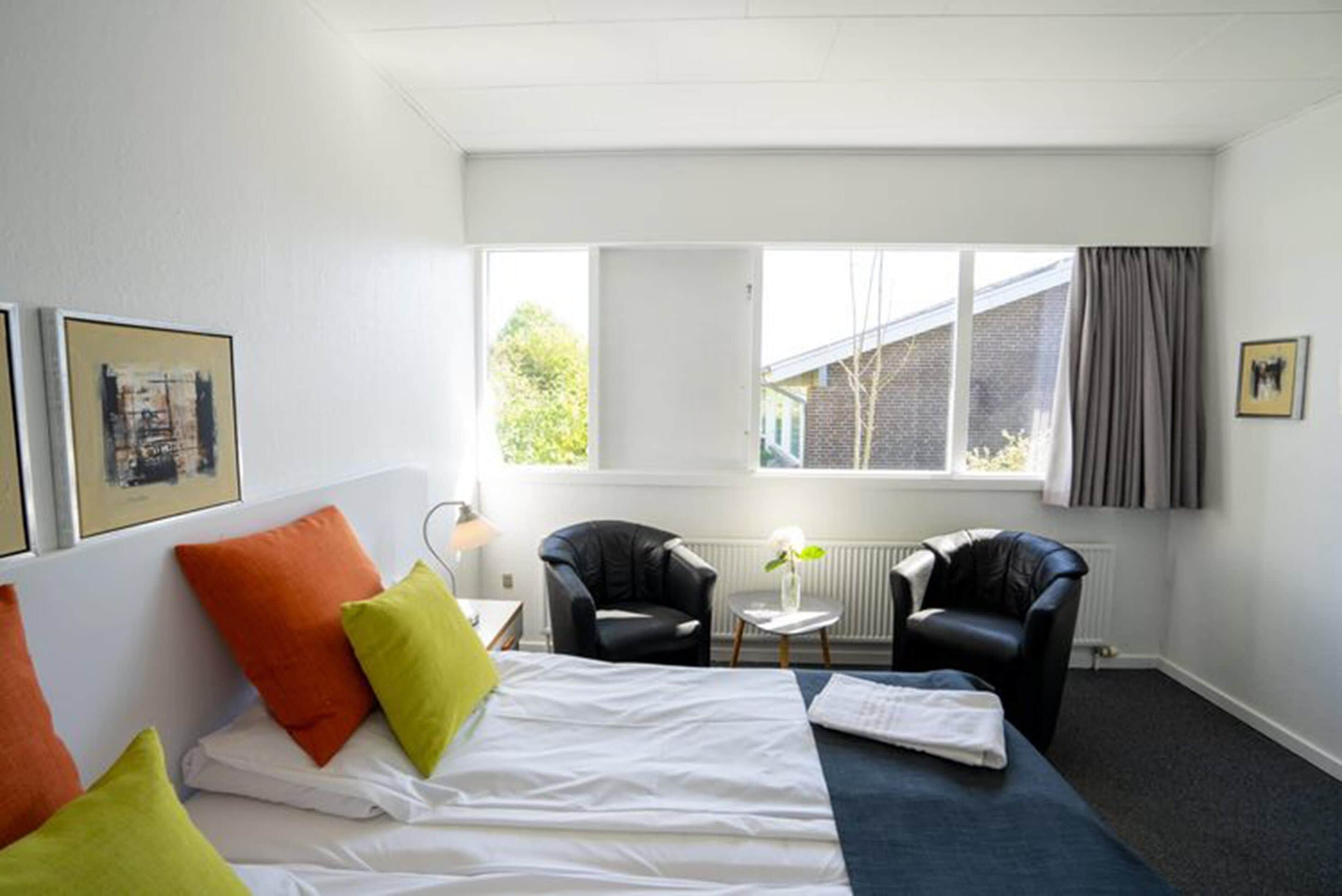 A hotel room with a bed, two chairs, a small table, and a window with a view of a building and trees.