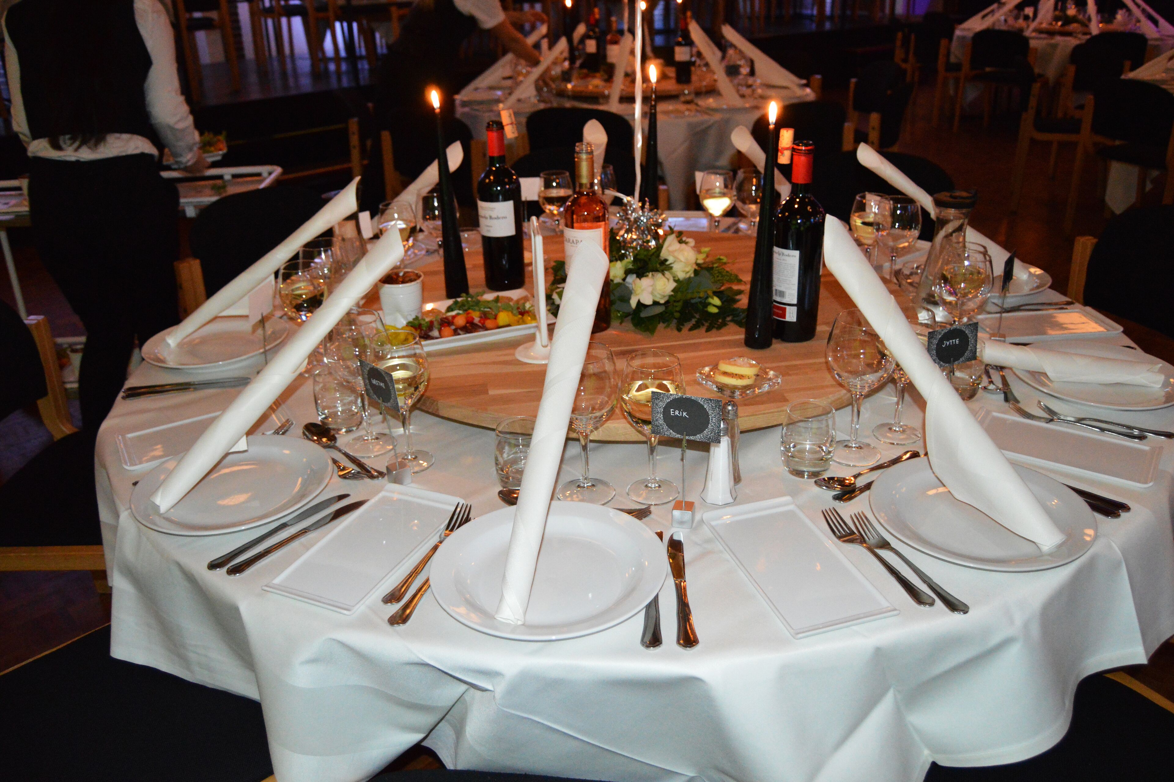 A formal dining table set for a meal with multiple wine bottles, glasses, and a centerpiece.
