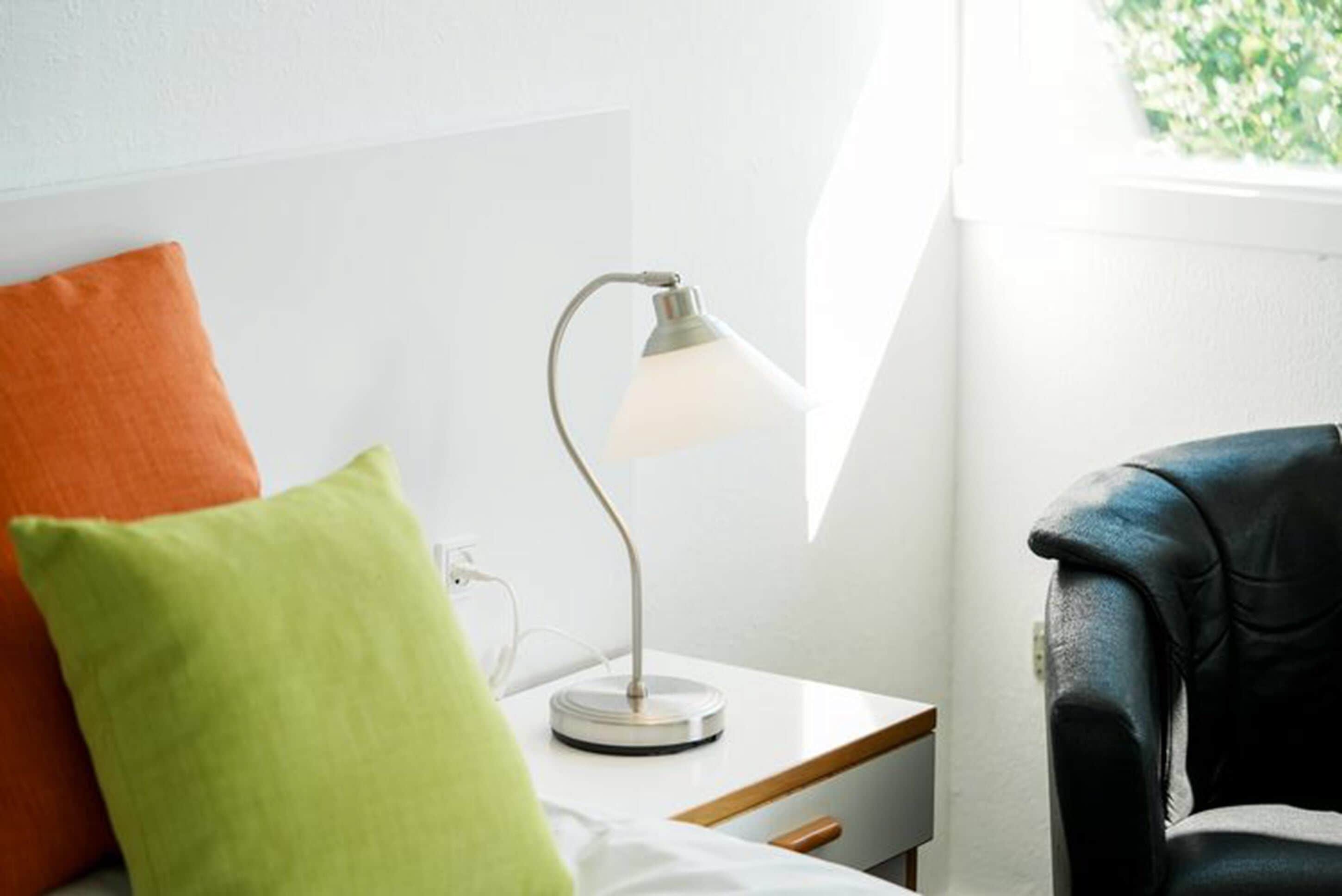 Un dormitorio ordenado con una mesita de noche, una lámpara y dos almohadas.