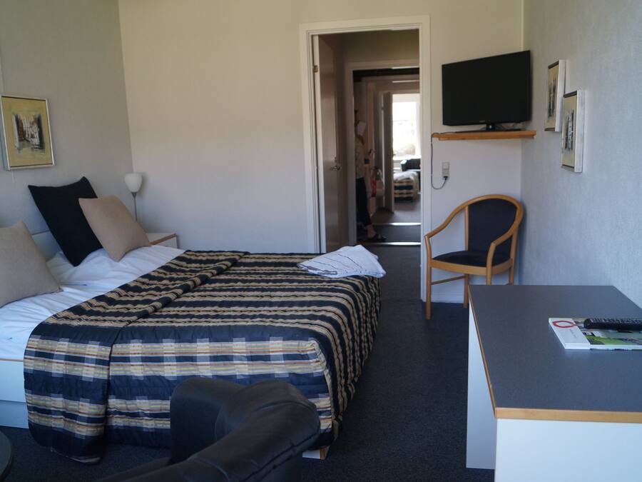 Quarto de hotel com cama, escrivaninha, cadeira, televisão e obras de arte nas paredes.