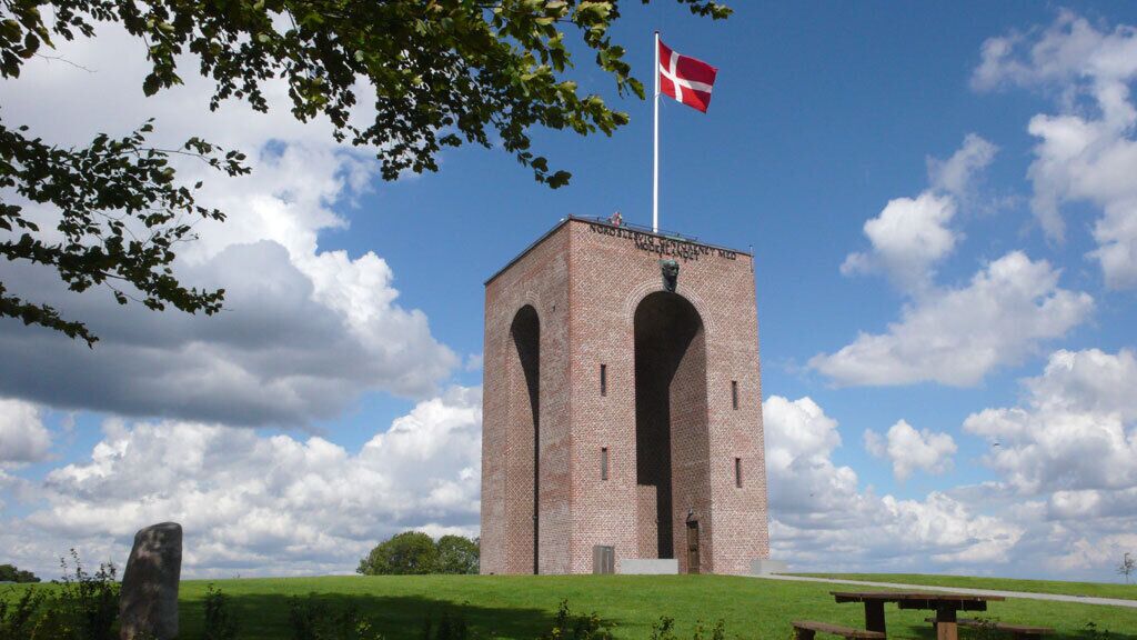 A brick tower with a flag, surrounded by a grassy area and a picnic table.