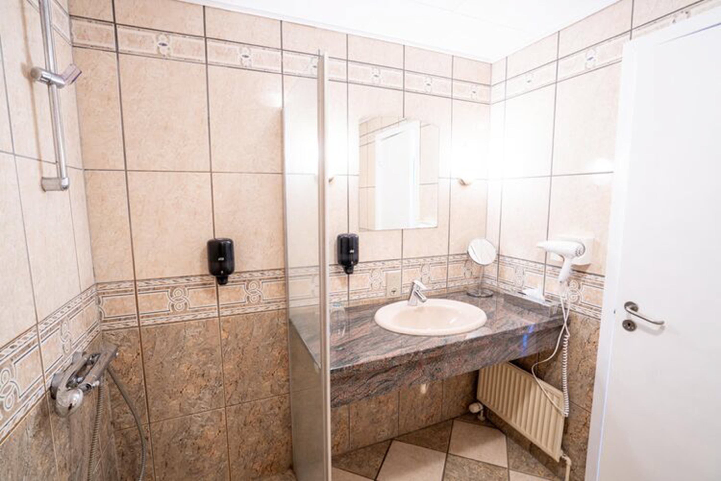 Um banheiro com pia de mármore, chuveiro manual, porta-toalhas e espelho.