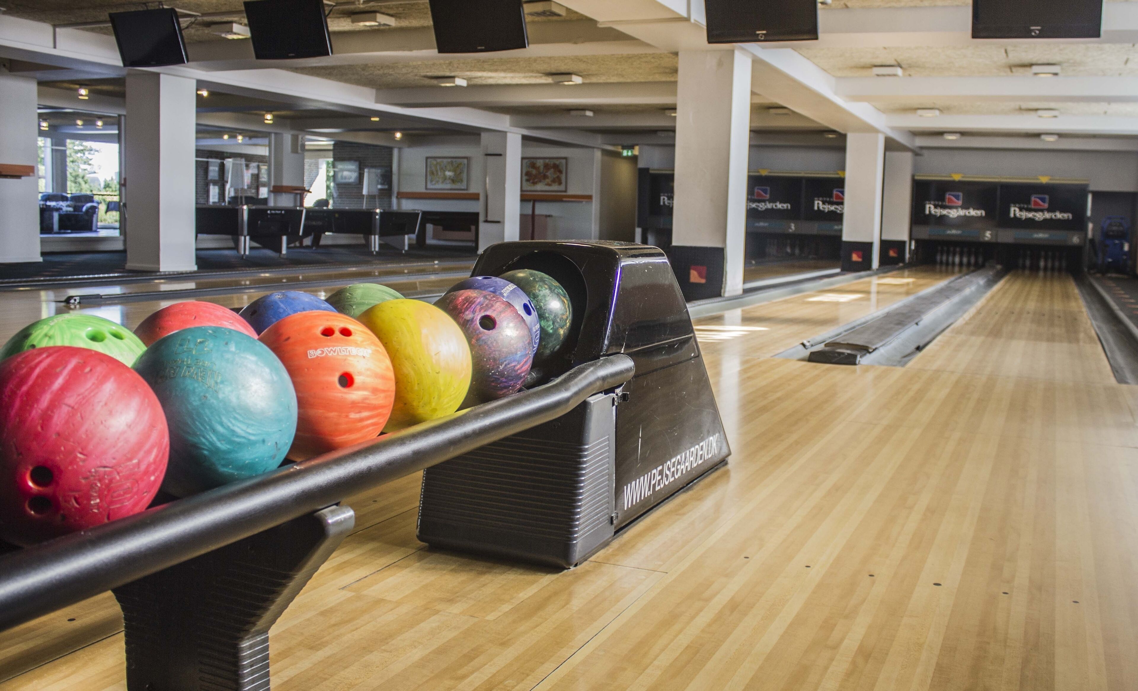 A bowling alley with multiple lanes, a bowling ball rack, and a wooden floor.