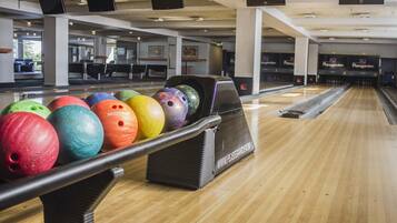 A bowling alley with multiple lanes, a bowling ball rack, and a wooden floor.