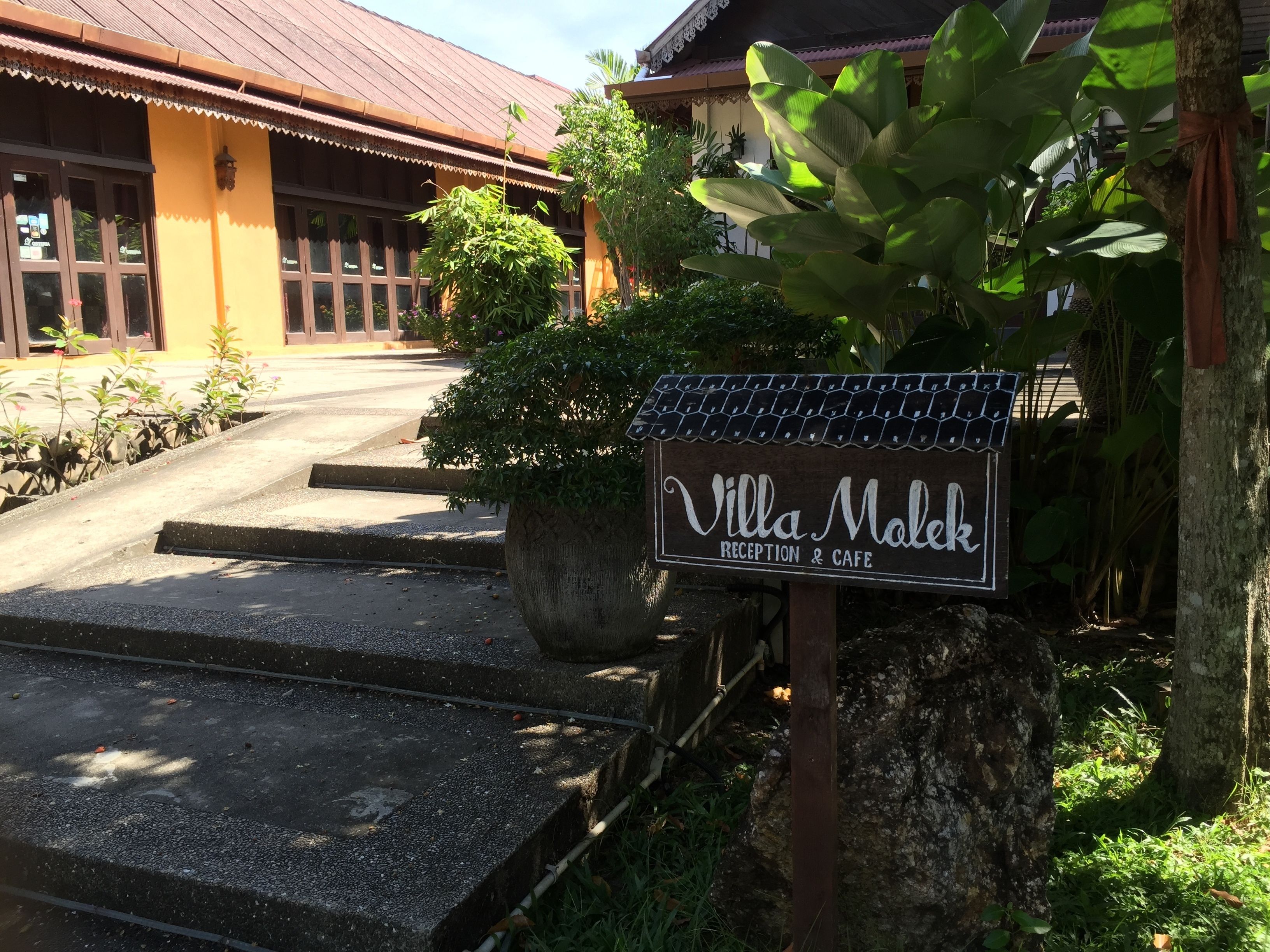 A sign for Villa Malek Reception & Cafe with a concrete staircase leading up to the entrance.