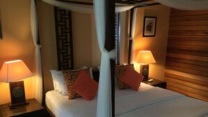 A four-poster bed with white linens, two nightstands with lamps, and a wooden headboard. - Villa Molek (Langkawi)