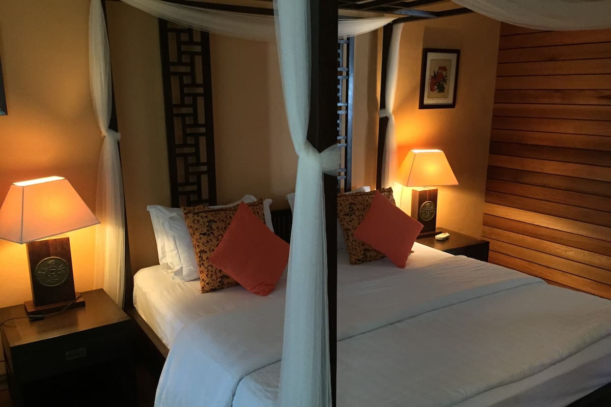 A four-poster bed with white linens, two nightstands with lamps, and a wooden headboard.