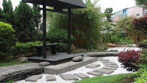 Un jardín con un pabellón, un camino de piedra y diversas plantas.