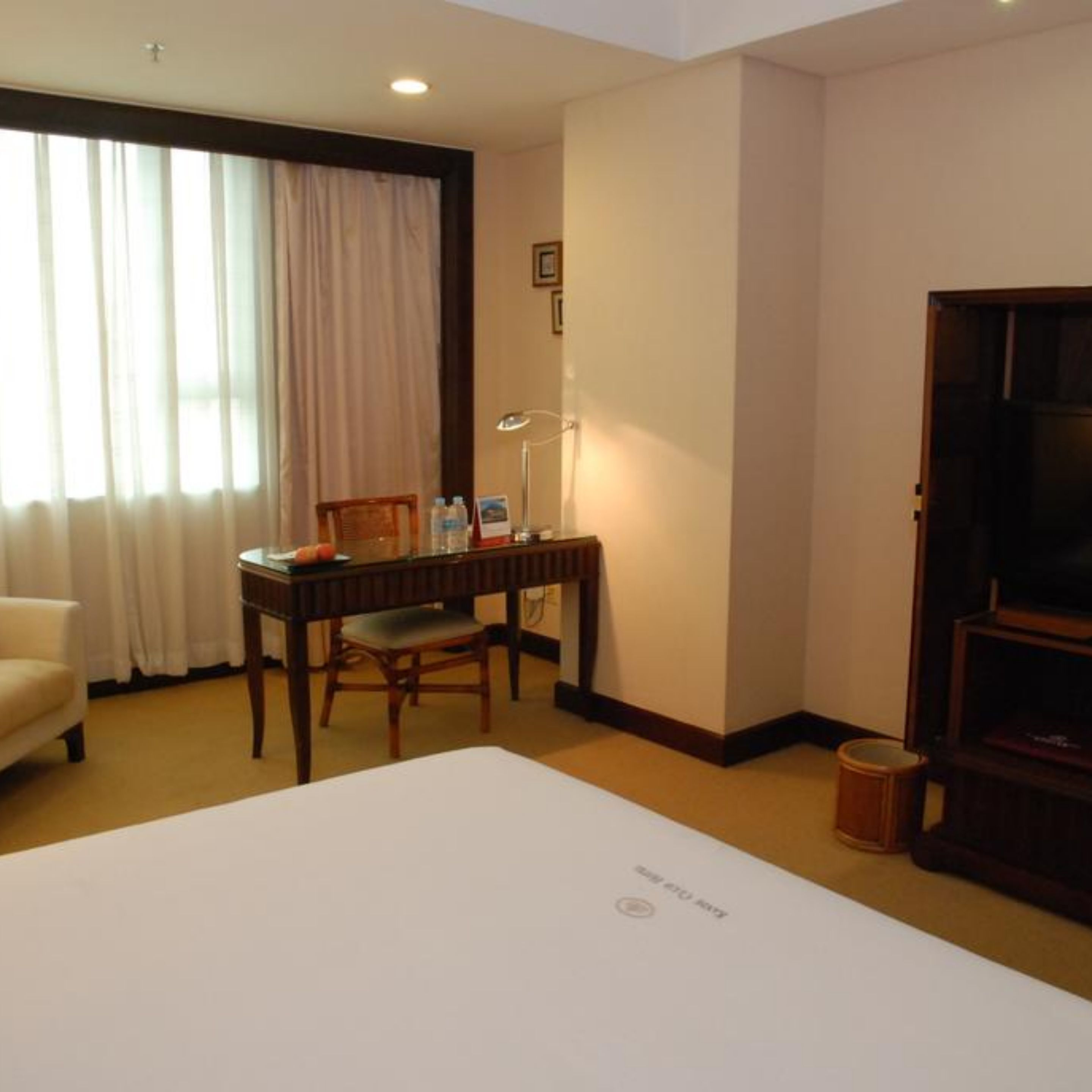 Quarto de hotel com cama, escrivaninha com cadeira, televisão e janela com cortinas.