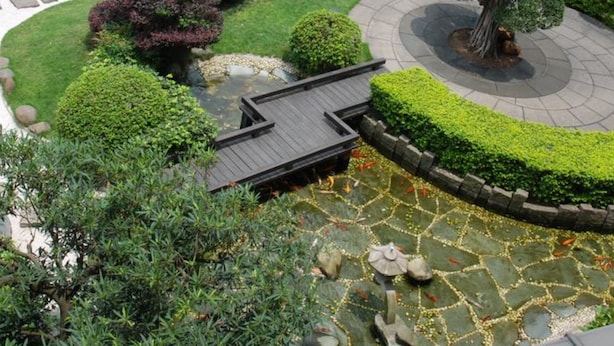 Un jardín cuidadosamente diseñado con un estanque central, senderos de piedra y diversas formas de topiaria.