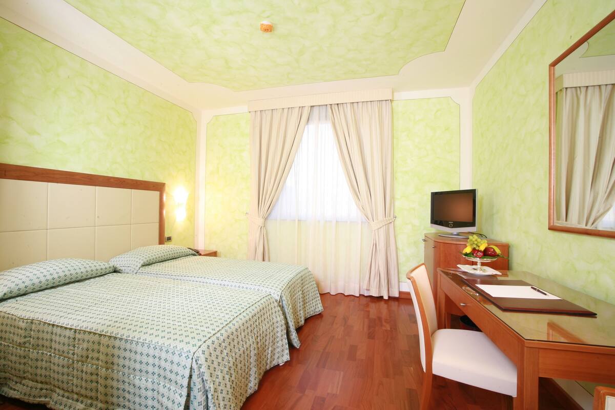 Habitación de hotel con dos camas, un escritorio, una silla, un televisor y una ventana con cortinas.