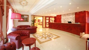 A hotel lobby with a red reception desk, plush red seating, and a decorative ceiling. - Grand Hotel del Parco - Bergamo Airport (Stezzano)
