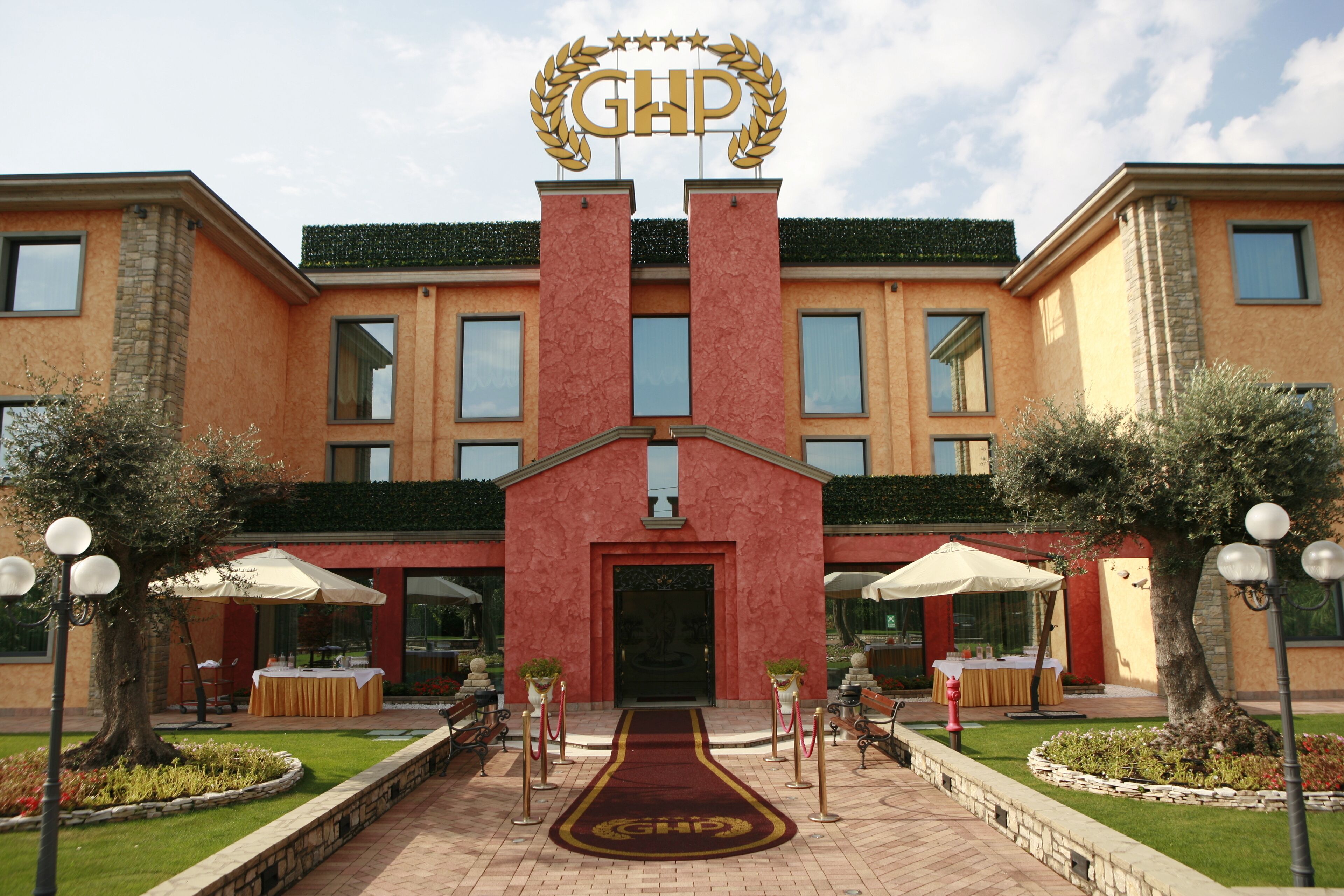 A hotel entrance with a red facade, a central entrance, and a sign with 'GHP' above.