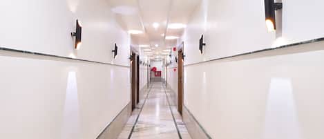Un largo pasillo bien iluminado, con suelo de mármol y lámparas fijadas a la pared.