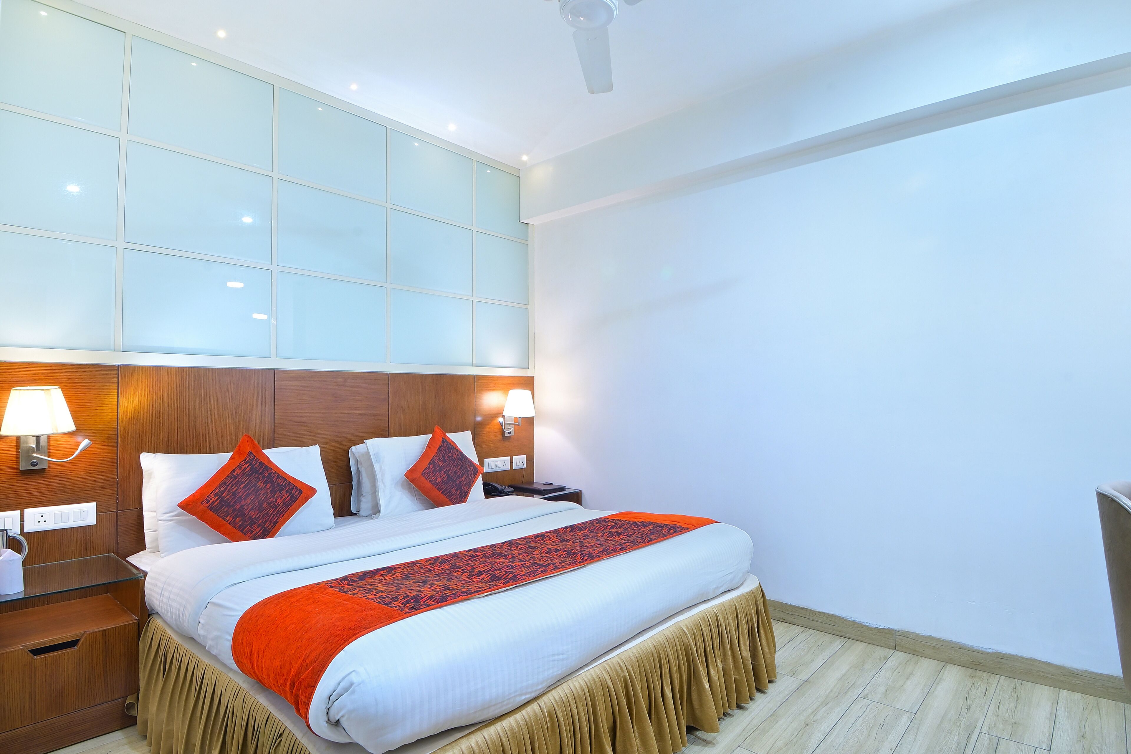 A hotel room with a large bed, wooden headboard, bedside lamps, and a view of the city.