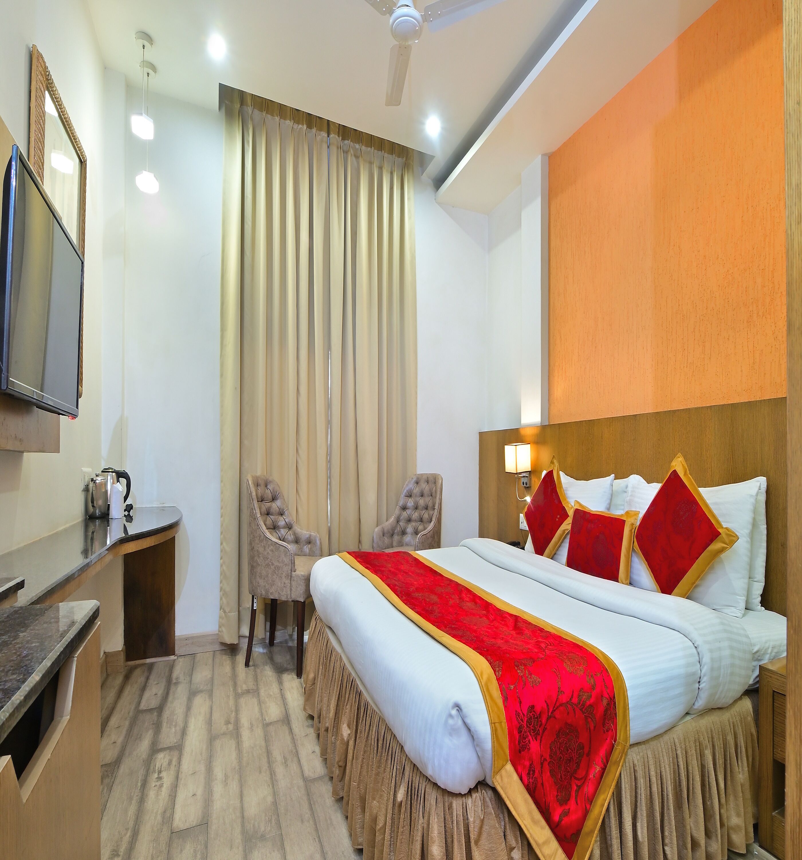 A hotel room with a bed, two chairs, a desk, a television, and a window with curtains.
