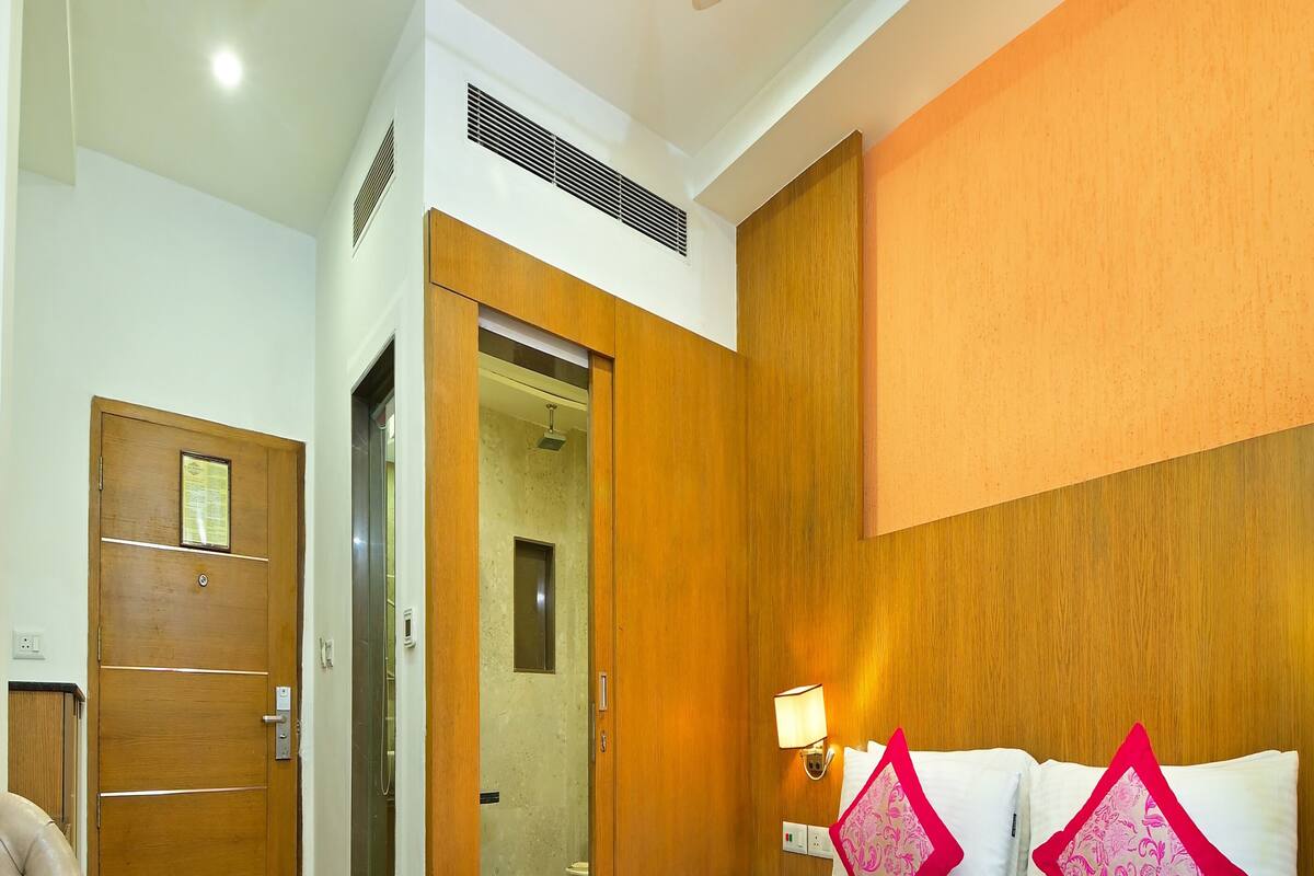 A hotel room with a bed, a wooden wardrobe, a seating area with a chair, and a small table.