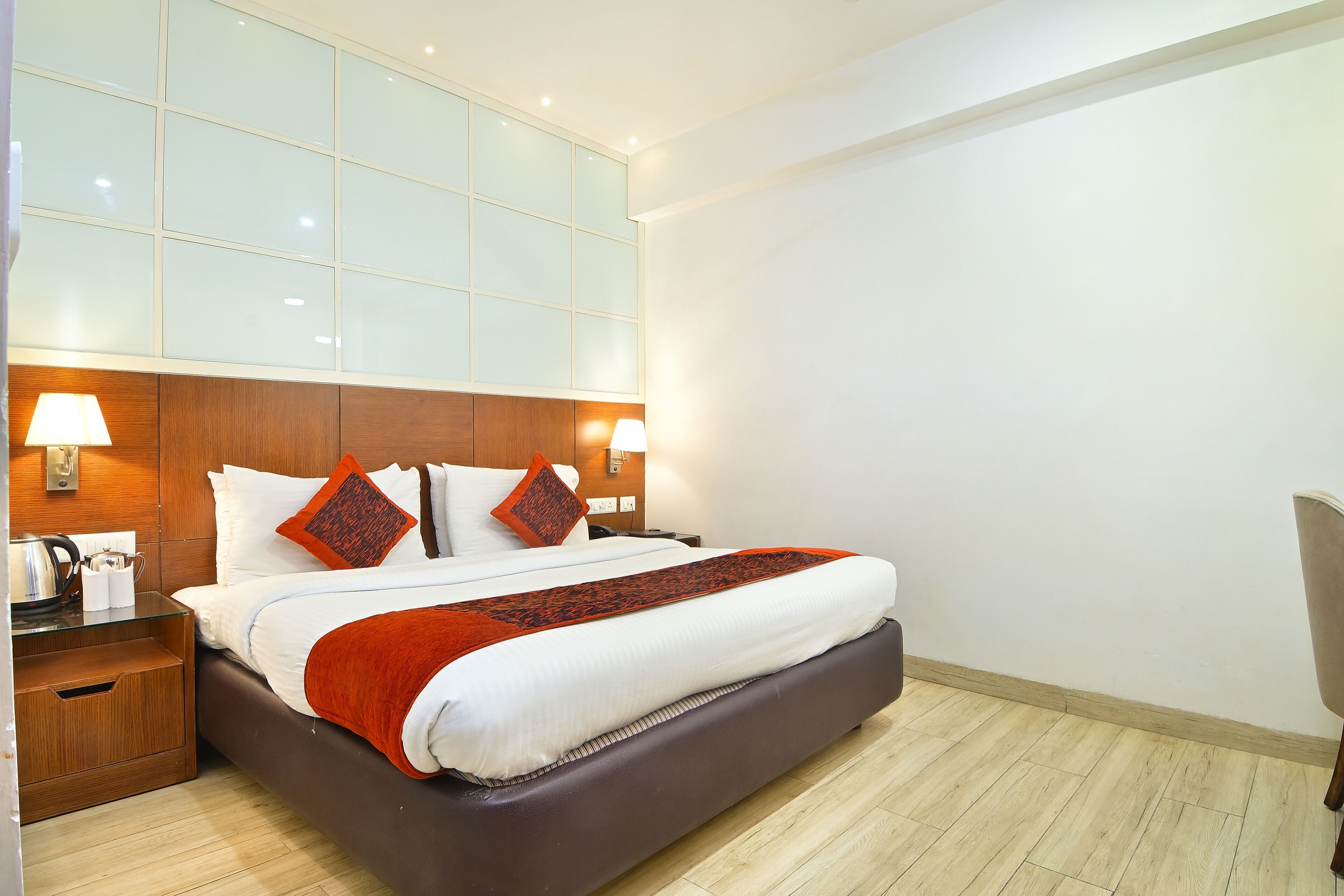 Een hotelkamer met een groot bed, een houten hoofdbord, twee bedlampjes, een nachtkastje en een glazen bijzettafeltje.