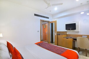 A hotel room with a bed, a desk, a chair, a television, and a ceiling fan.