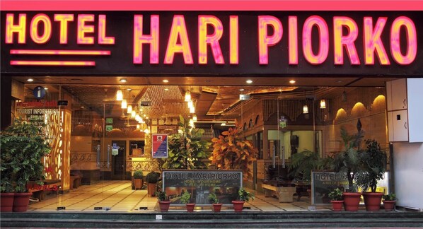 Exterior del Hotel Hari Piorko con un letrero de neón, una recepción y plantas en macetas.