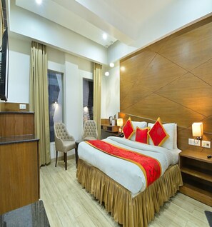 Habitación de hotel con una cama, dos sillas, una mesita de noche, una lámpara y un cabecero de madera.