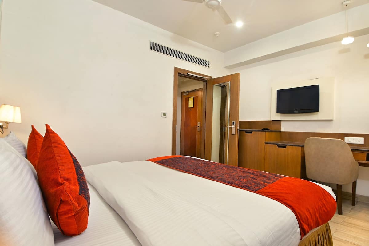 A hotel room with a bed, a desk, a chair, a television, and a door.