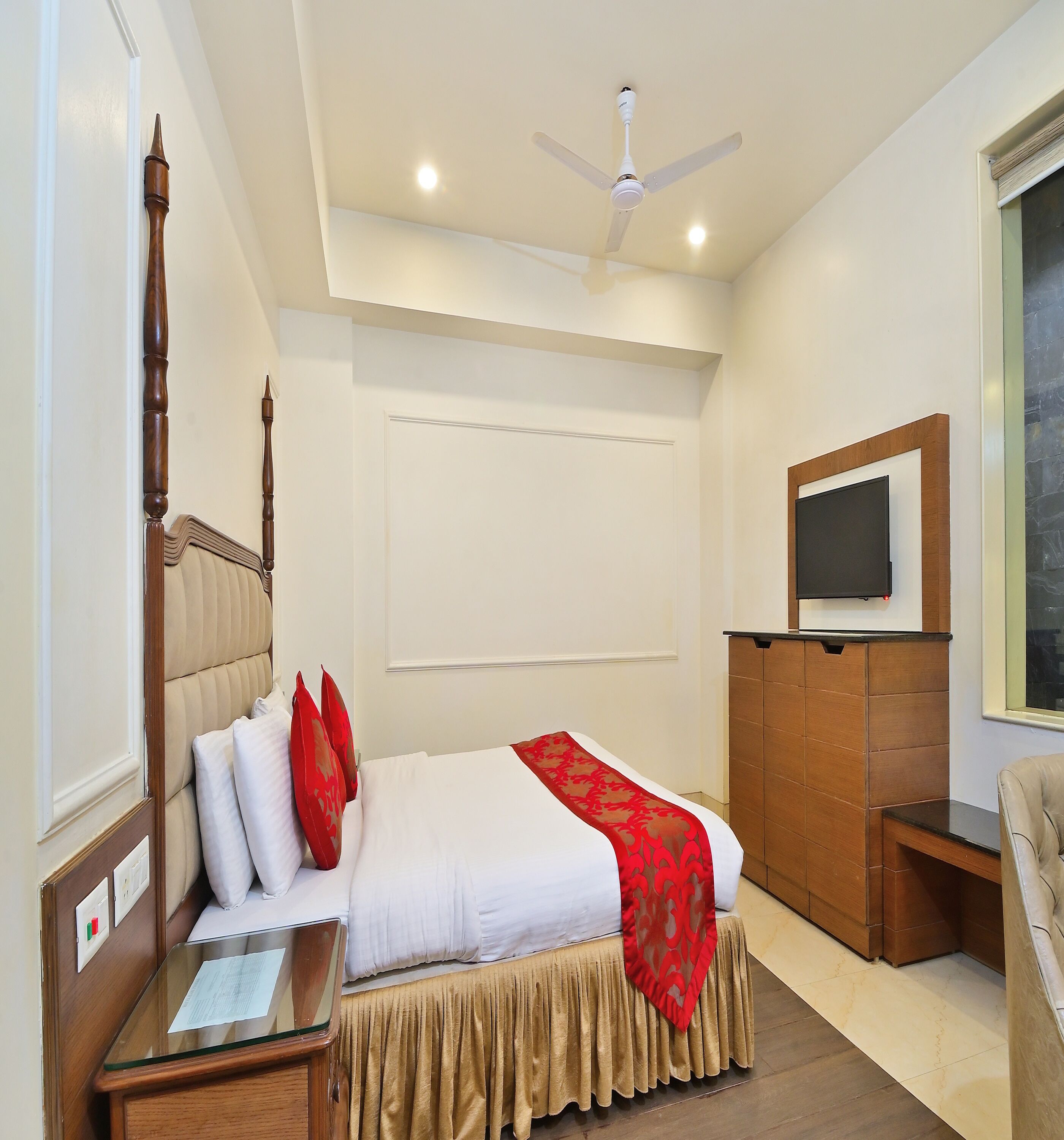 A hotel room with a bed, a wooden nightstand, a television on a wooden cabinet, and a ceiling fan.