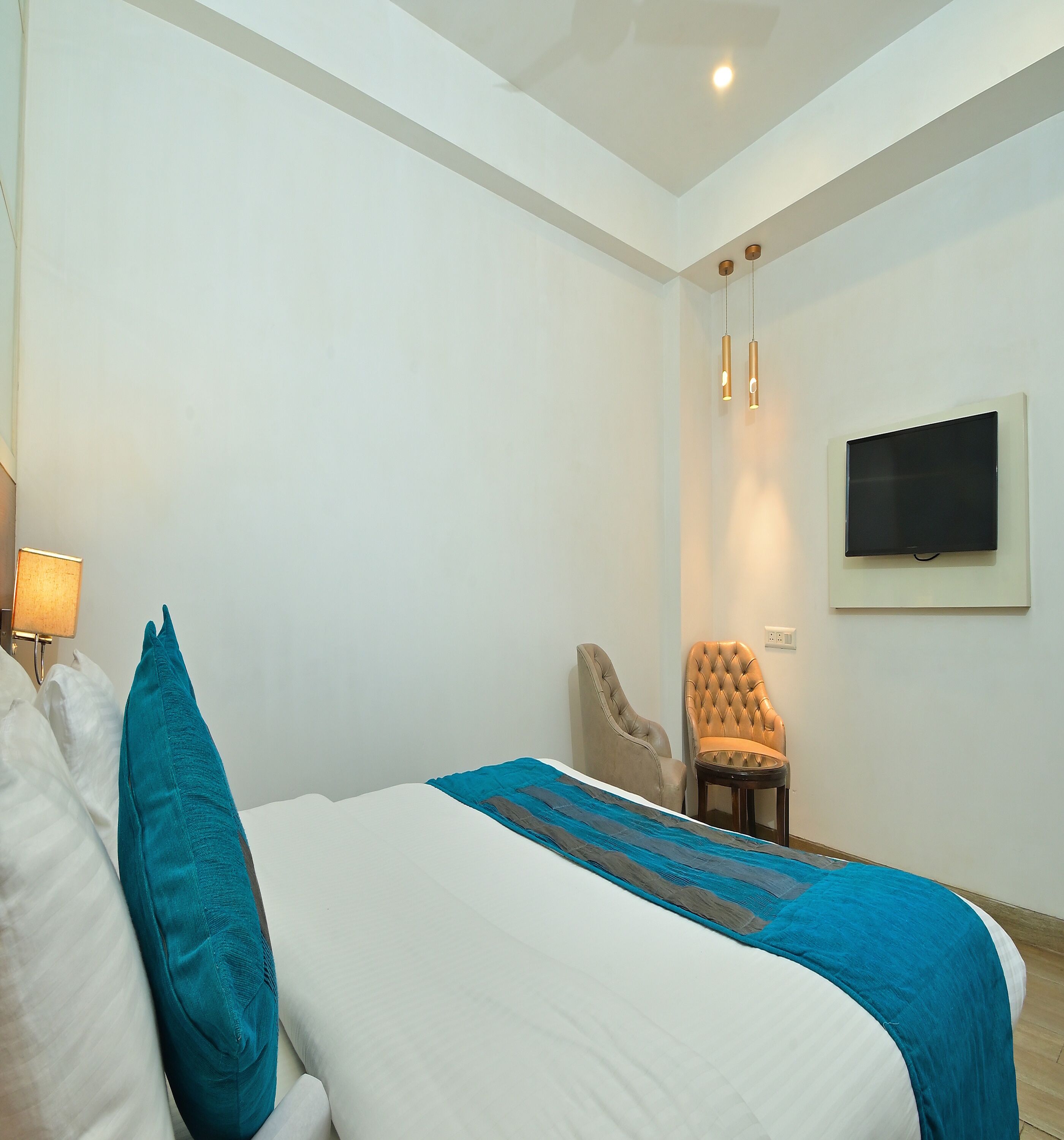 A hotel room with a bed, a chair, a TV mounted on the wall, and a ceiling light fixture.