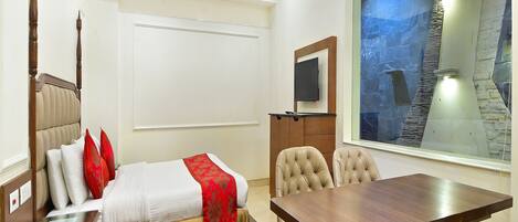 Habitación de hotel con cama, escritorio, silla, televisor y ventana grande con vistas a una estructura de piedra.