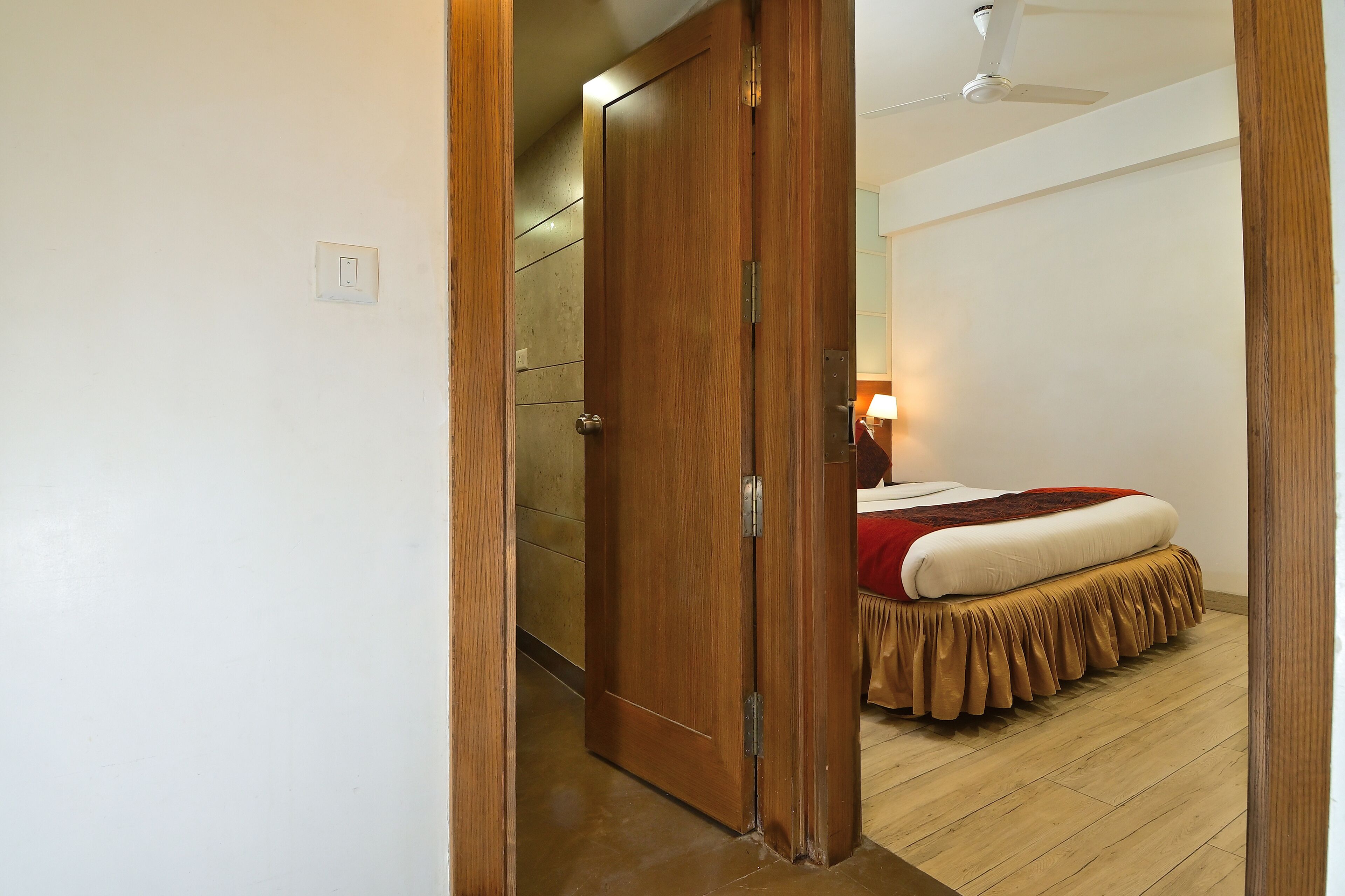 A wooden door leading to a bedroom with a bed, a ceiling fan, and a light fixture.