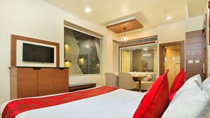 Ein Hotelzimmer mit einem großen Bett, einem an der Wand befestigten Fernseher, einem Schreibtisch mit Stuhl und einem Fenster mit Blick auf die Stadt.