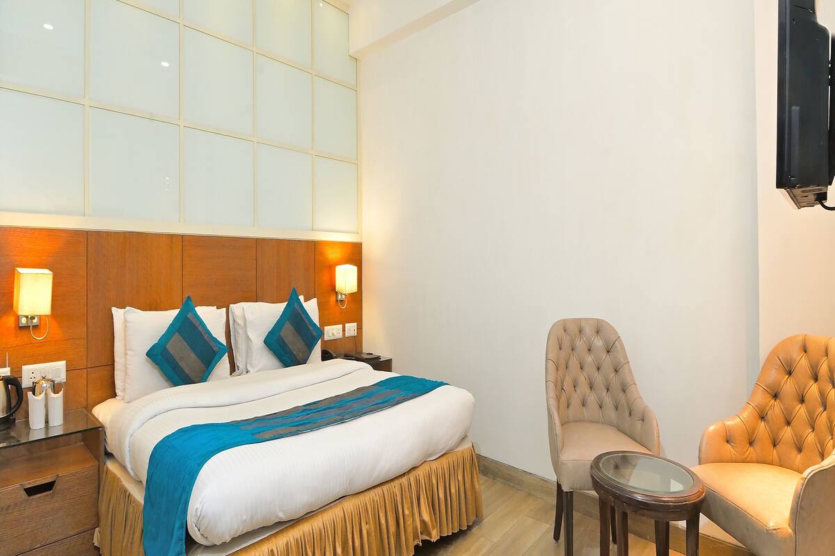 A hotel room with a large bed, a wooden headboard, a ceiling fan, a TV mounted on the wall, and a small round table.