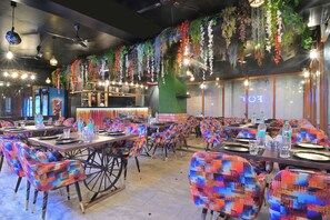Un restaurante con sillas de colores, mesas dispuestas con platos y vasos, y plantas colgantes.