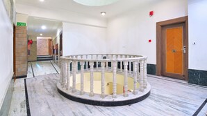 Eine Lobby mit Marmorboden, einer zentralen runden Empfangstheke, einer Holztür und einer Treppe mit Glastrennwand.