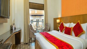 Ein Hotelzimmer mit Bett, Schreibtisch, Stuhl, Fernseher und einem Fenster mit Vorhängen.
