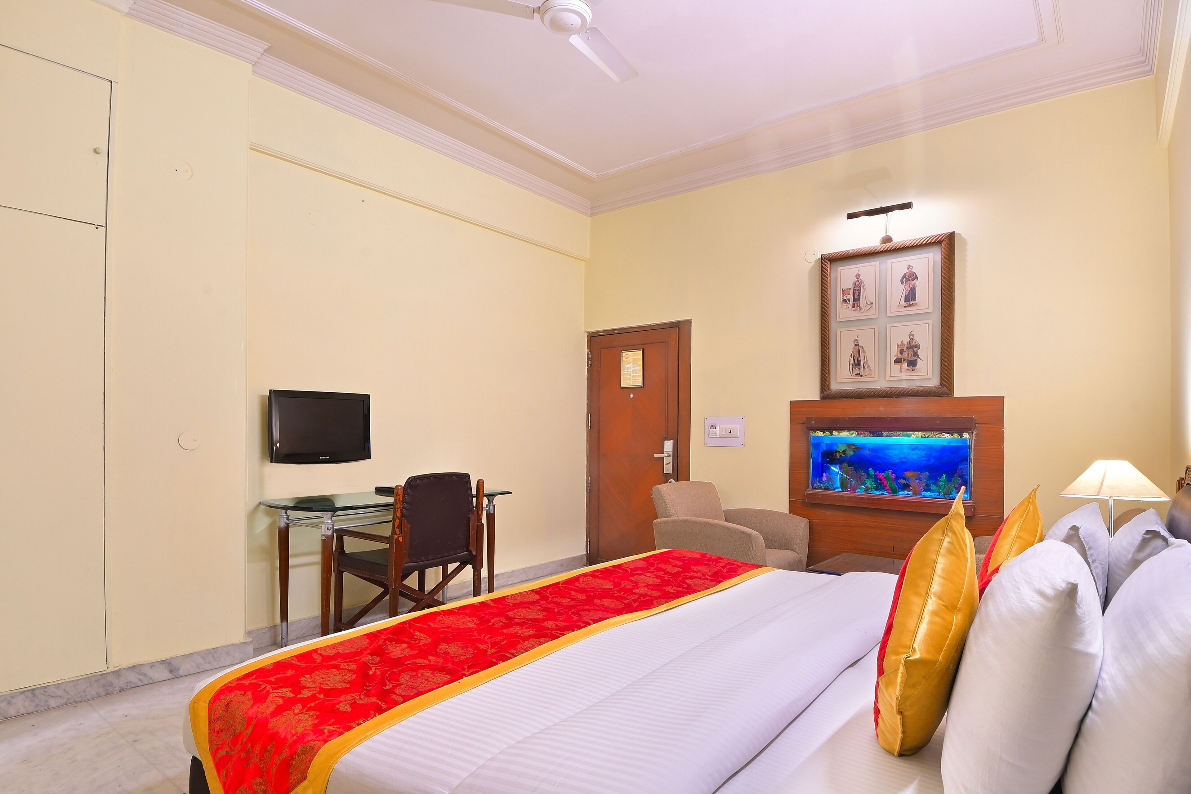 A hotel room with a bed, a desk, a television, a fish tank, and a door.
