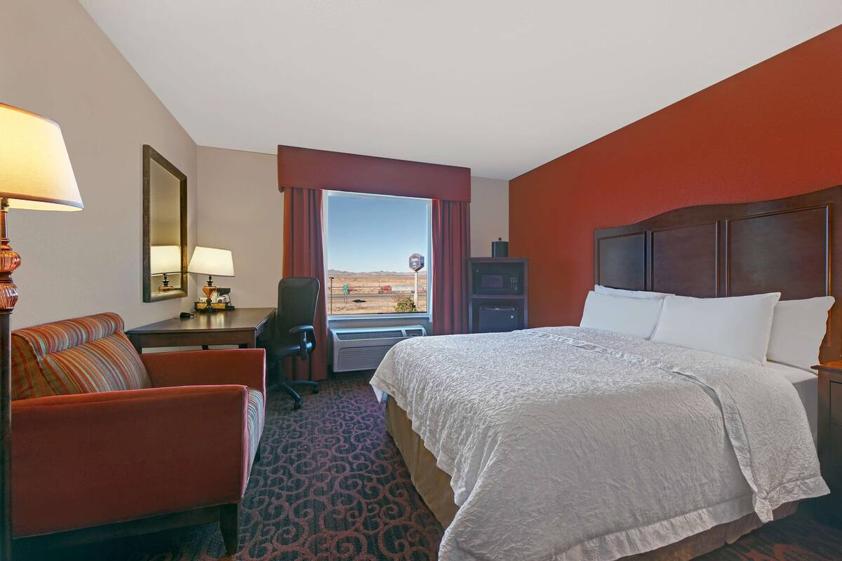 A hotel room with a large bed, a desk with a lamp, a chair, and a view of the desert.
