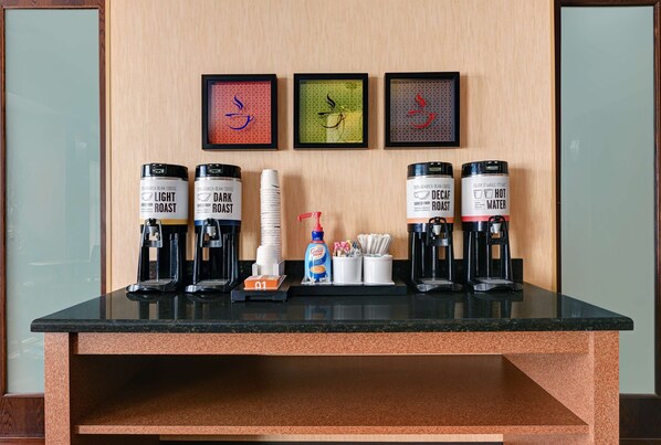 A coffee station with two coffee makers, a stack of white cups, a bottle of coffee creamer, and a coffee grinder.
