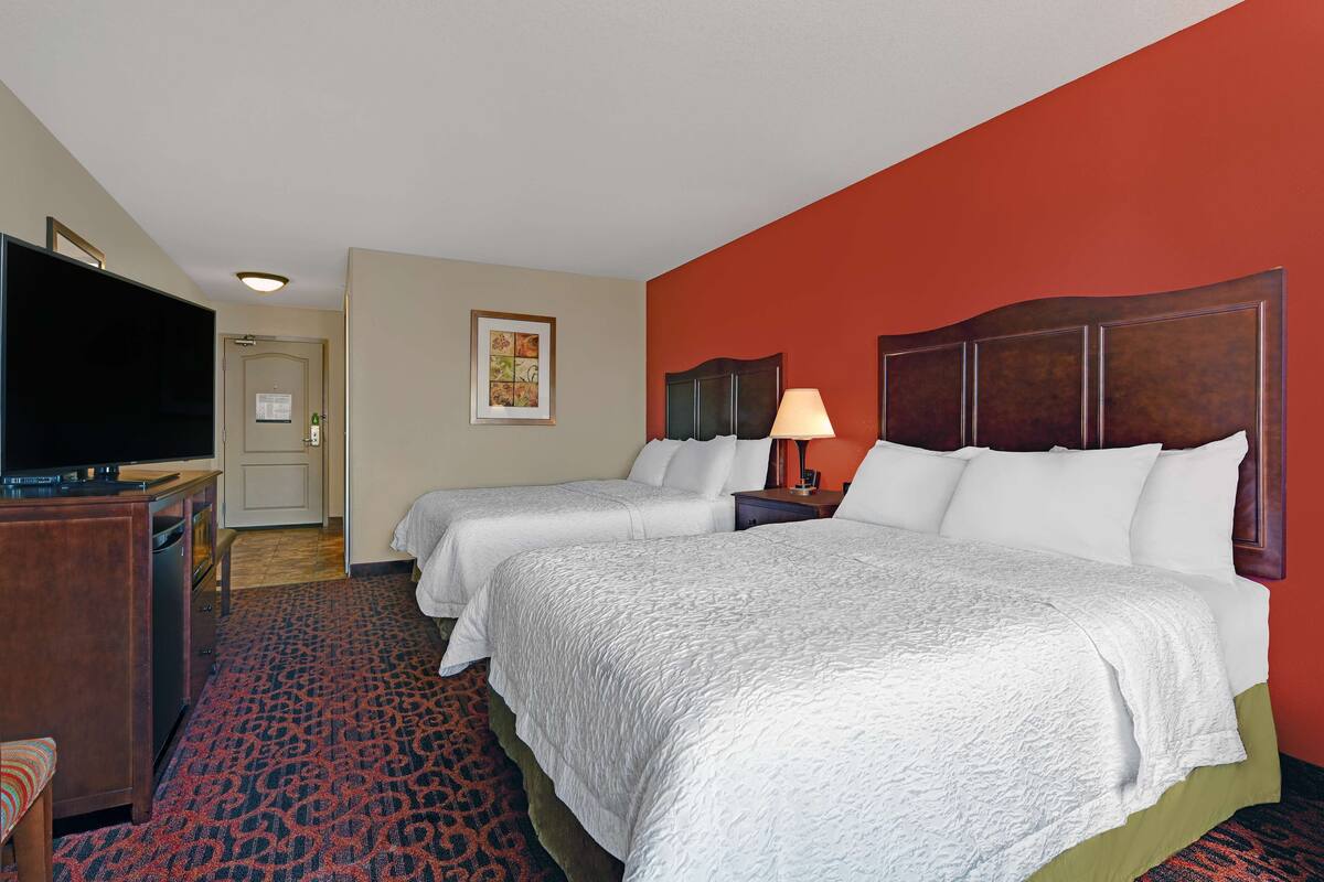 A hotel room with two beds, a TV, a desk, and a red accent wall.