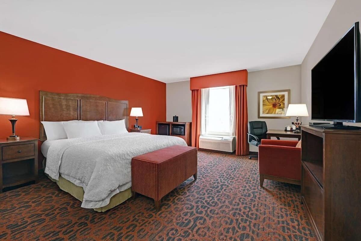 A hotel room with a bed, a desk, a TV, and a window with curtains.