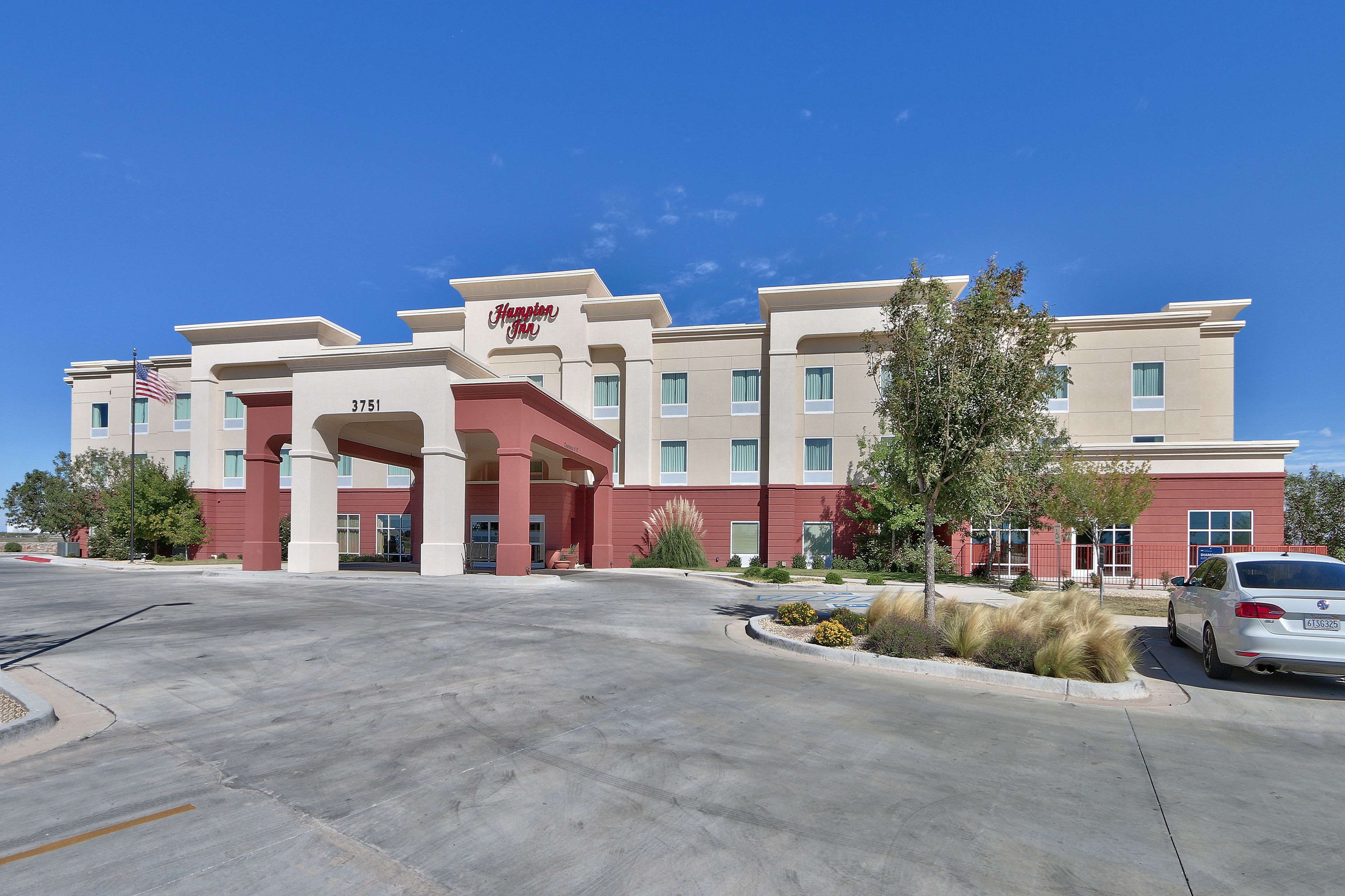 A hotel with a red and beige facade, a clear blue sky, and a parking lot.