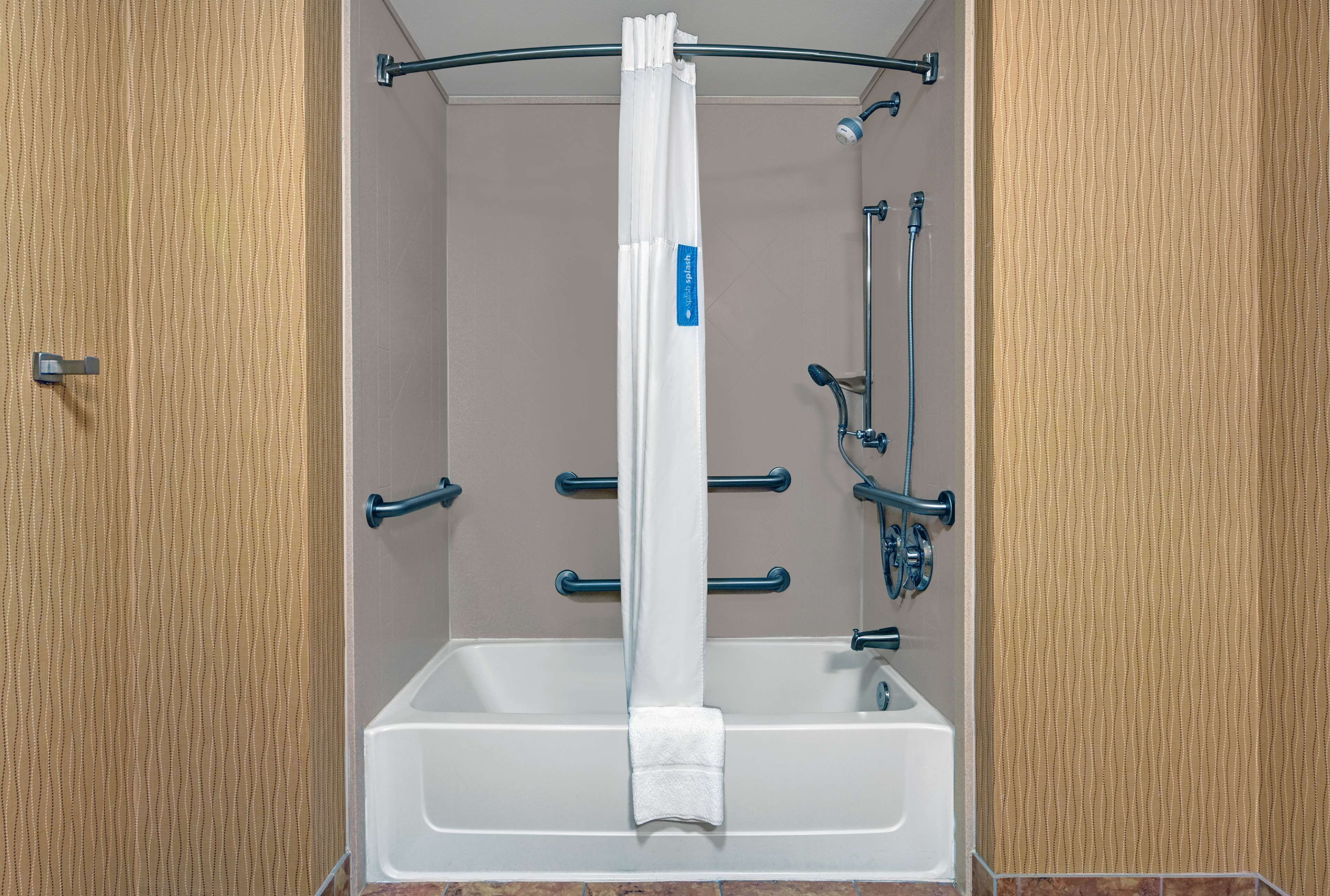 Une cabine de douche avec un rideau blanc, une douchette à main et un robinet à main.