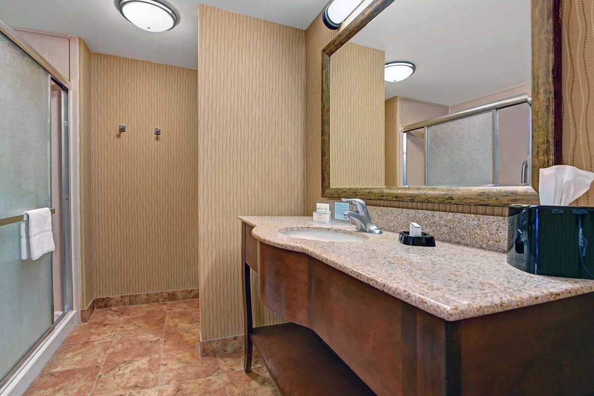 A bathroom with a granite countertop, a mirror, a towel rack, and a shower area.