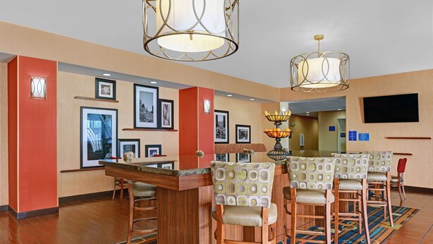 A hotel lobby with a bar area, multiple framed pictures on the walls, and a television mounted on the wall. - Hampton Inn Deming (Deming)